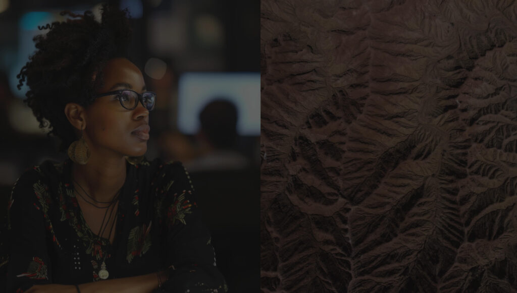 A woman with glasses and large earrings sits attentively in a dimly lit environment, with a blurred background of people and
