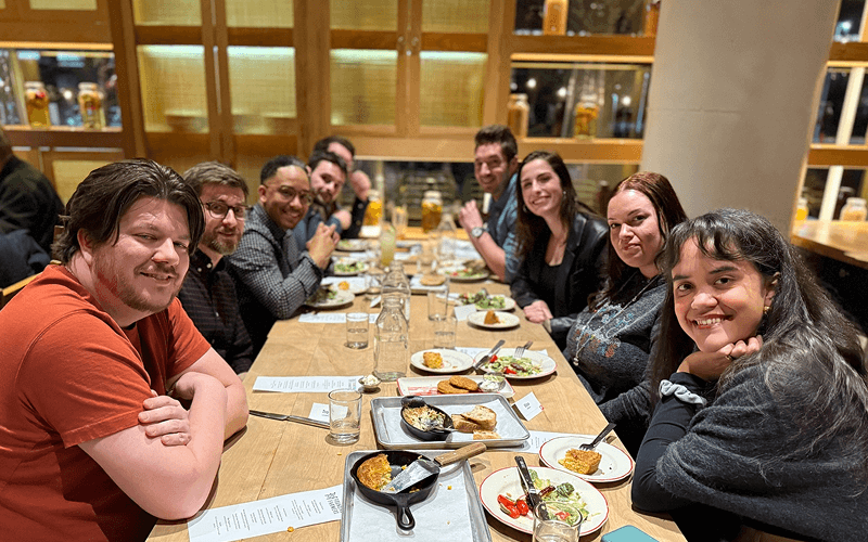 Punch Team Culture Photo-14 A group of nine people sitting at a long table in a restaurant, enjoying a meal together and smiling at the camera.