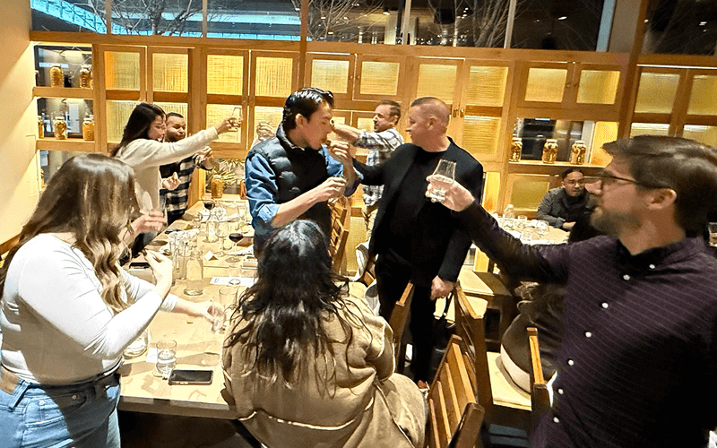 Punch Team Culture Photo-15 People are celebrating around a dining table, raising glasses and toasting in a lively, joyful gathering.
