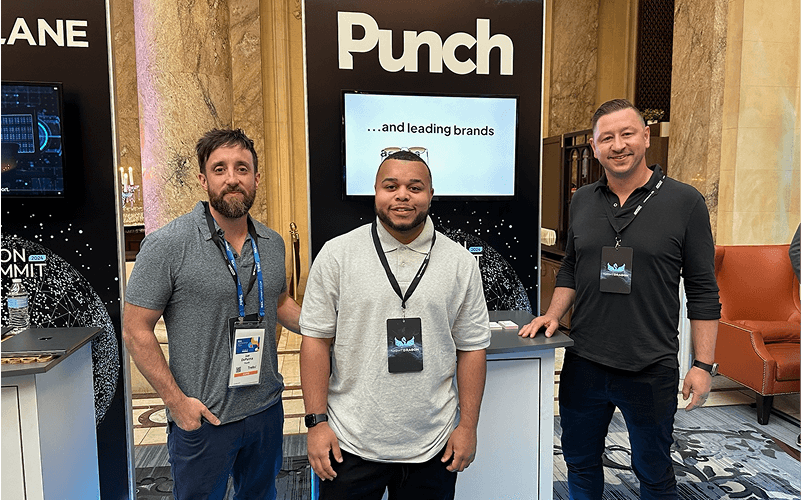 Punch Team Culture Photo-16 Three men stand in front of a "Punch" display at a conference, smiling and wearing conference badges.