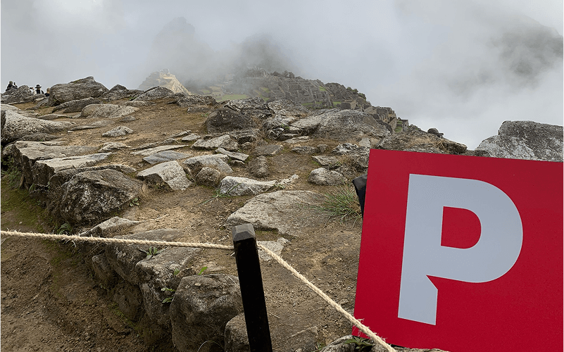 Punch Team Culture Photo-18 A rocky mountain trail with a "P" parking sign and a rope barrier, partially obscured by clouds and fog.