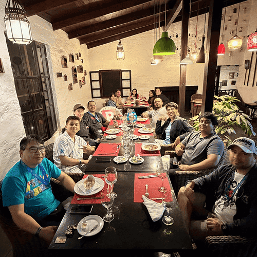 Punch Team Culture Photo 19 A group of people seated around a long dining table with red placemats, plates, glasses, and a bottle of water in a cozy,