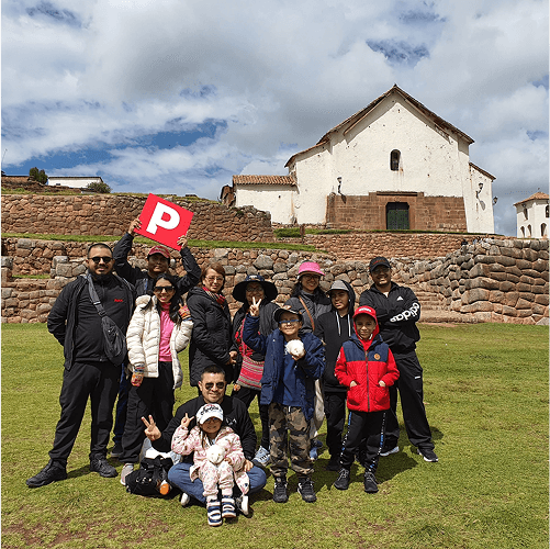 Punch Team Culture Photo-19 A group of people, including children, pose outdoors in front of an old white church with a stone foundation under a cloudy