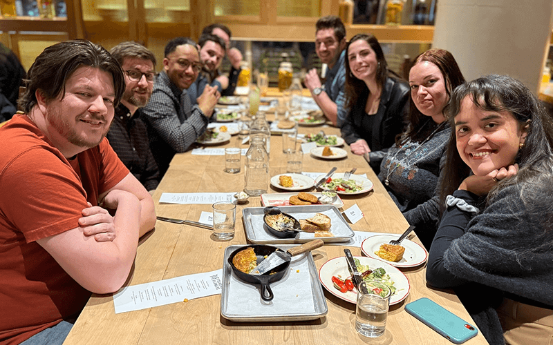 Punch Team Culture Photo-21 A group of people sit around a long table enjoying a meal together in a cozy restaurant setting.