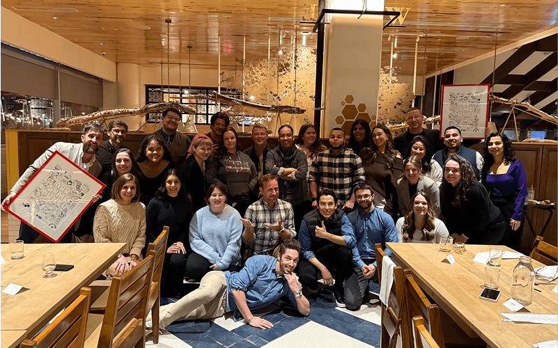 Punch Team Culture Photo-24 A group of 24 people gathered together in a restaurant, posing for a photo with some smiling and others making gestures.