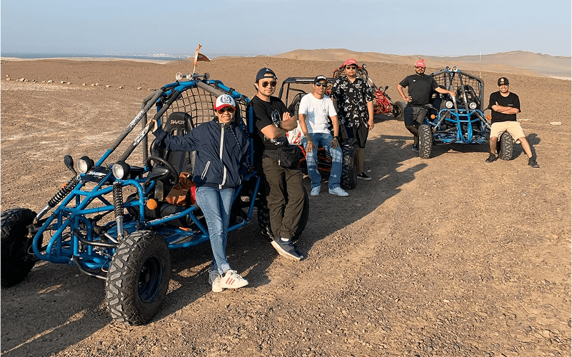 Punch Team Culture Photo-25 A group of seven people stands next to off-road dune buggies in a desert landscape under a clear sky.