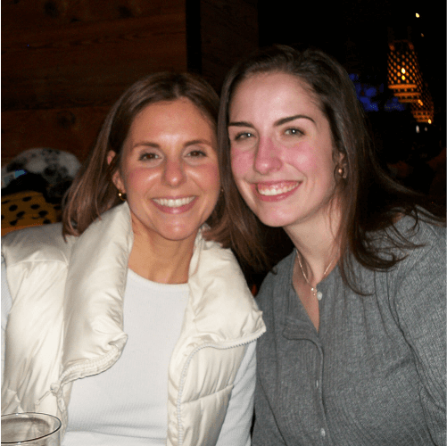 Punch Team Culture Photo-28 Two women with brown hair and smiling faces pose closely together in a warmly lit indoor setting.