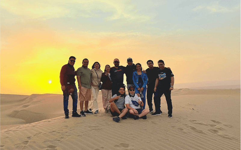 Punch Team Culture Photo-31 A group of ten people poses together on a desert dune at sunset.