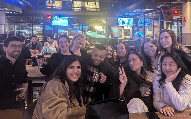 Punch Team Culture Photo-37 A group of friends smiling and posing together at a bar, some holding drinks and making peace signs.