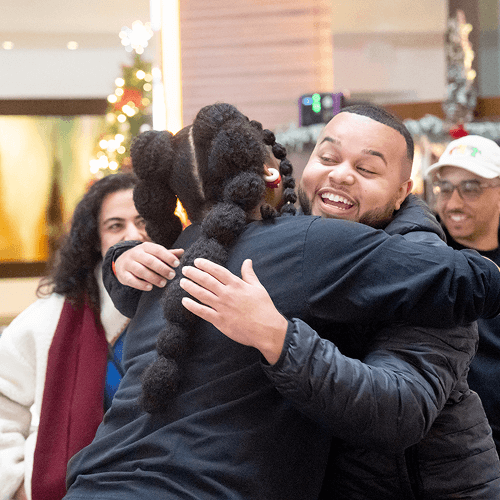 Punch Team Culture Photo 4 A man and woman embrace warmly while others smile in the background during a festive indoor gathering.