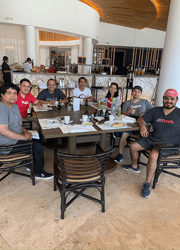 Punch Team Culture Photo-4 Six people sit around a table with food and drinks in a modern restaurant interior.