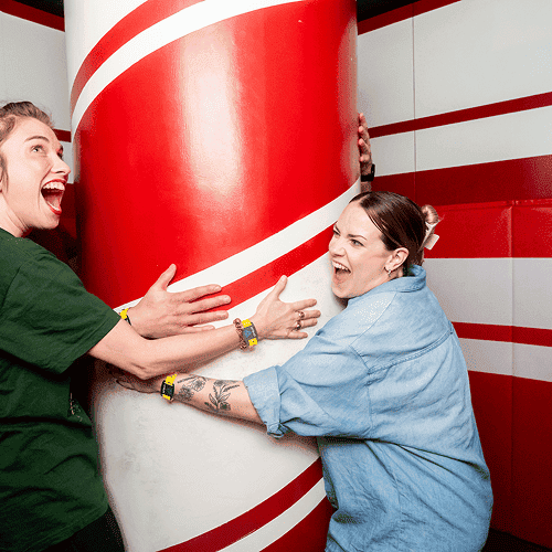 Punch Team Culture Photo 8 Two women are playfully hugging a large red and white striped pole, smiling and laughing.