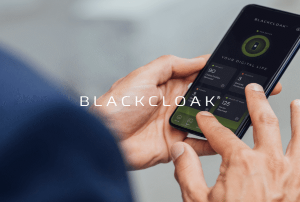 A person holds a smartphone displaying the BLACKCLOAK app with security status and device protection details.