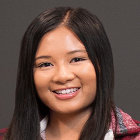 A young woman with straight black hair, smiling against a dark gray background.