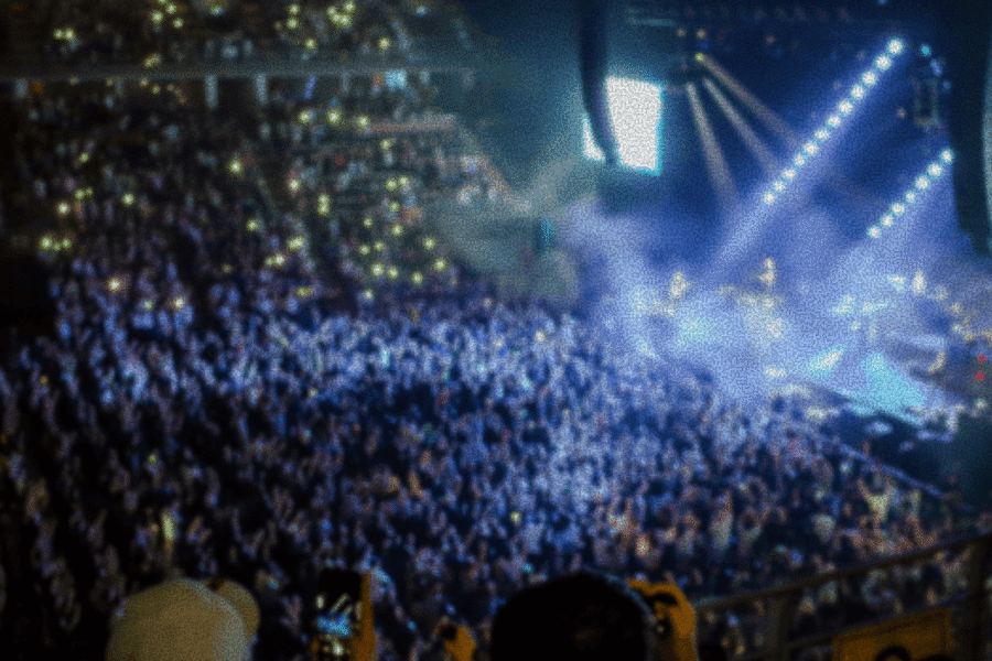 A large crowd at a concert with bright stage lights and smoke effects illuminating the scene.