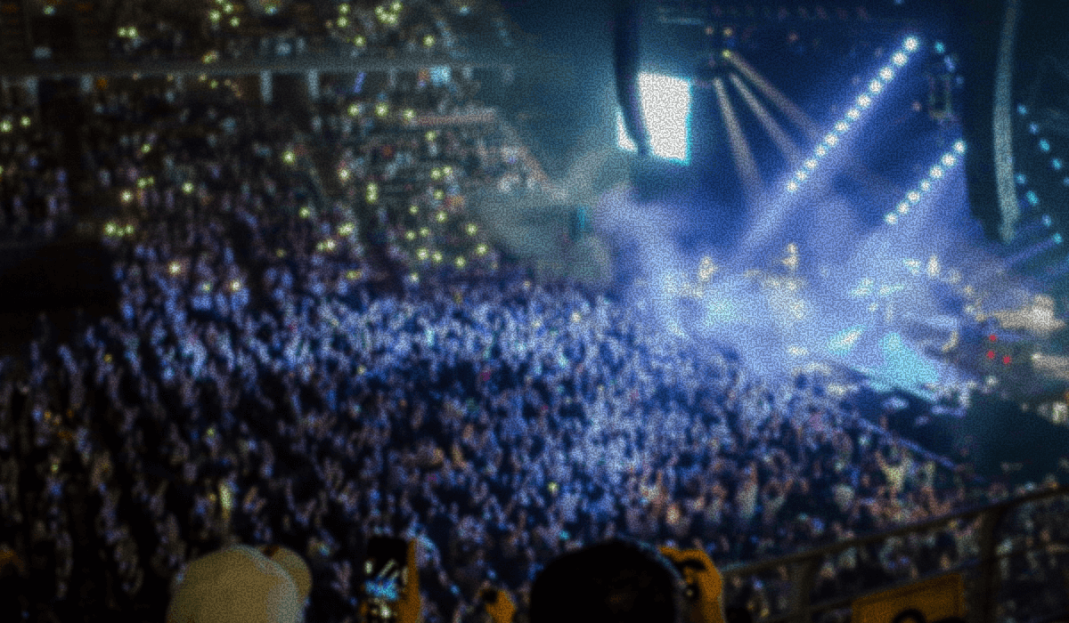 A large crowd at a concert with bright stage lights and smoke effects illuminating the scene.