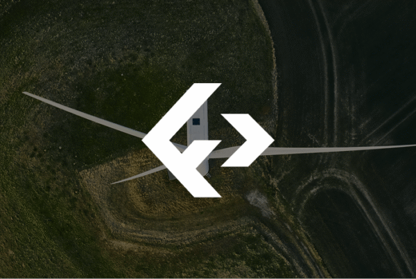 A drone captures an aerial view of a wind turbine with a large white logo overlay in the center, surrounded by green fields